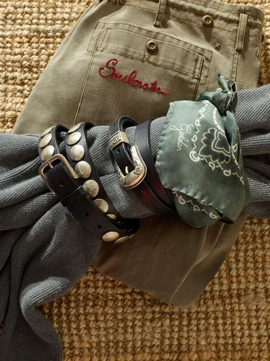 black-leather-belt-with-studs-rolled-up-over-a-blue-sweater-with-a-green-scarf-over-green-trousers